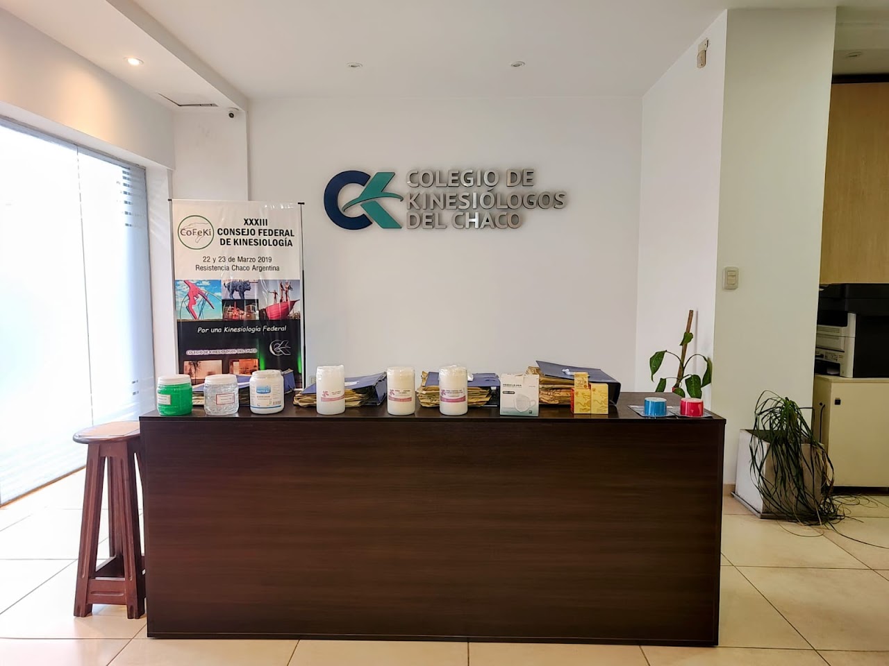 Interior reception and front desk lobby of an institutional professional association headquarters, modern minimalist wood accents, clean reception counter, comfortable waiting chairs, bright diffused architectural lighting, professional healthcare and collegiate administrative office.