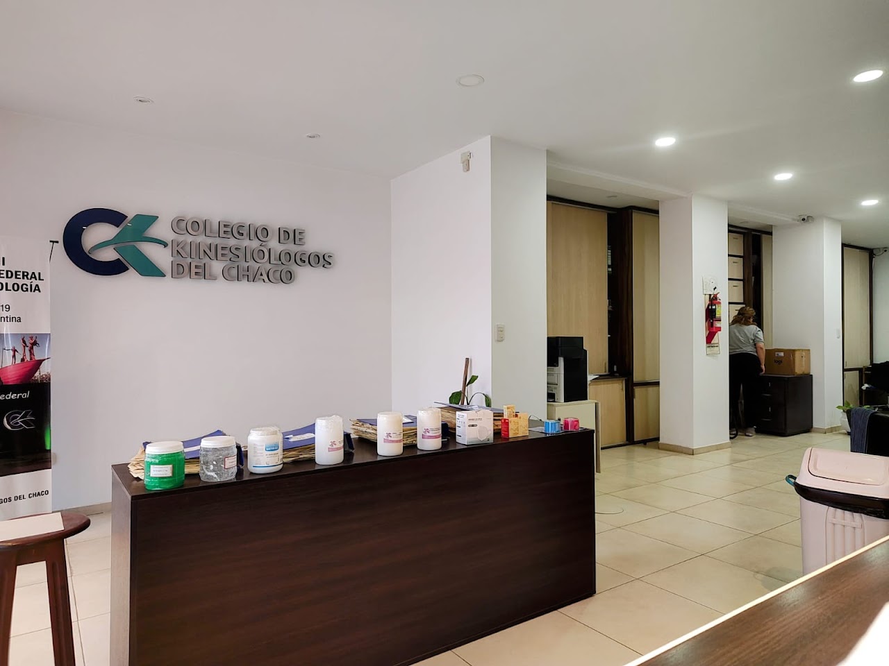 Modern consultation desk and administrative offices in an institutional college headquarters, clean glass partition, professional paperwork and certificates on wall, calm daylight, pristine interior.